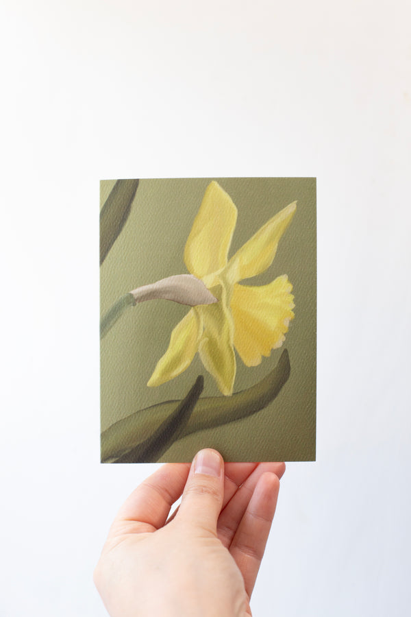 A Single Yellow Daffodil on a green background greeting card on textured paper.