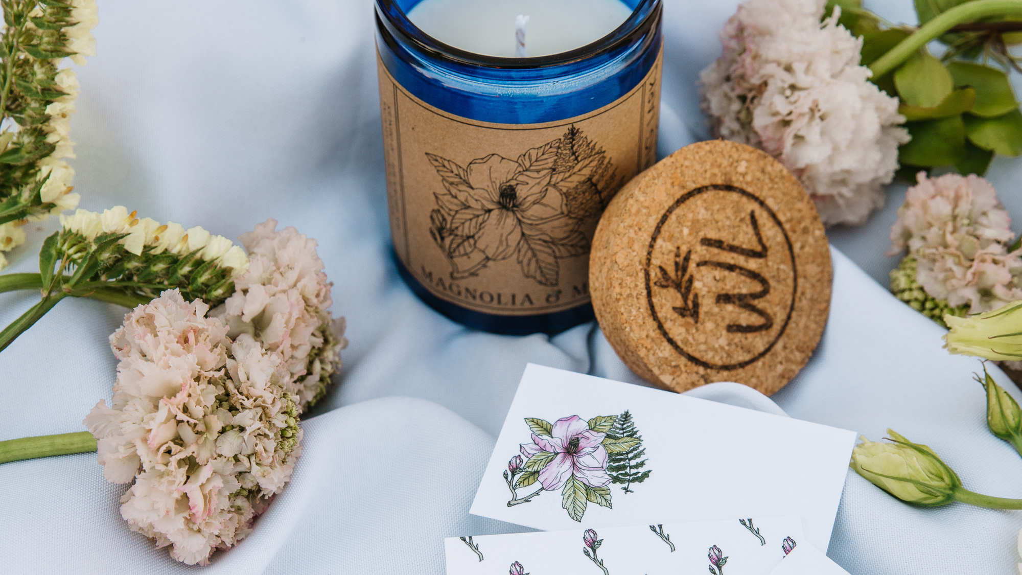 Magnolia & Moss Scented  Soy Candle with cork lid and flowers on a white background.