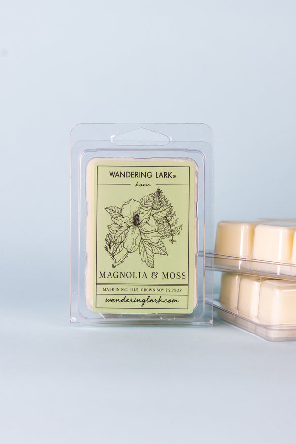Magnolia and moss wax melts in a clear container with a soft green label and illustration of a Magnolia and Fern.
