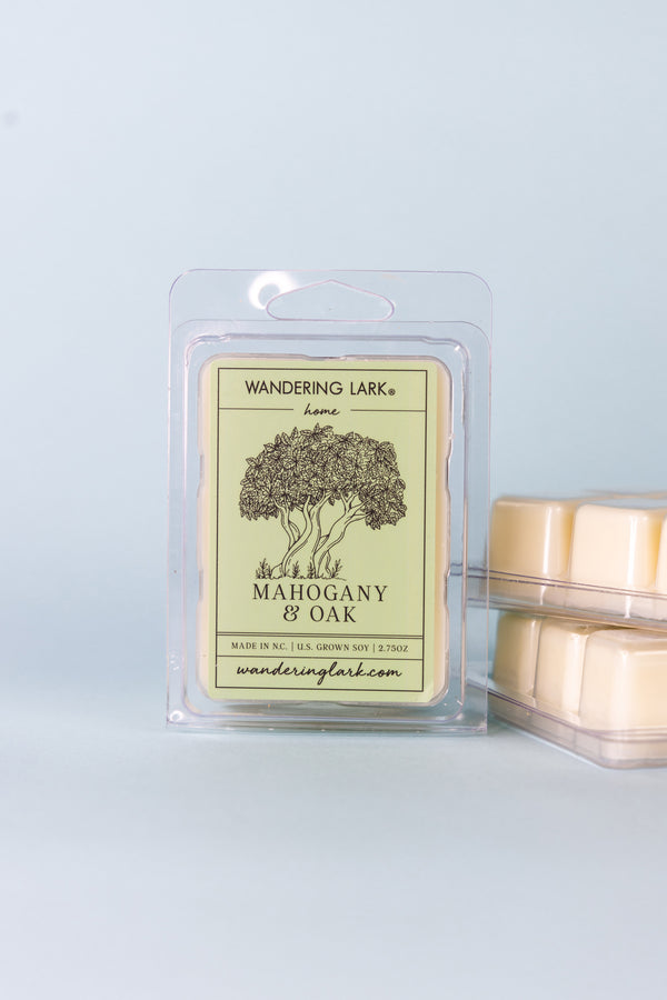 A package of 'Wandering Lark' brand wax melts with the scents of mahogany and oak. The package is clear, and the wax melts inside are visible, with a label that features a tree and the product name.