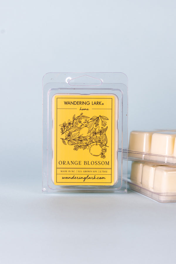 Orange Blossom Wax Melts in a Clear Container with an orange label with an illustration of oranges on a branch with blooms and leaves.