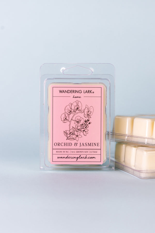 Orchid and Jasmine scented wax melts in a clear container with a pink label with an illustration of orchids.